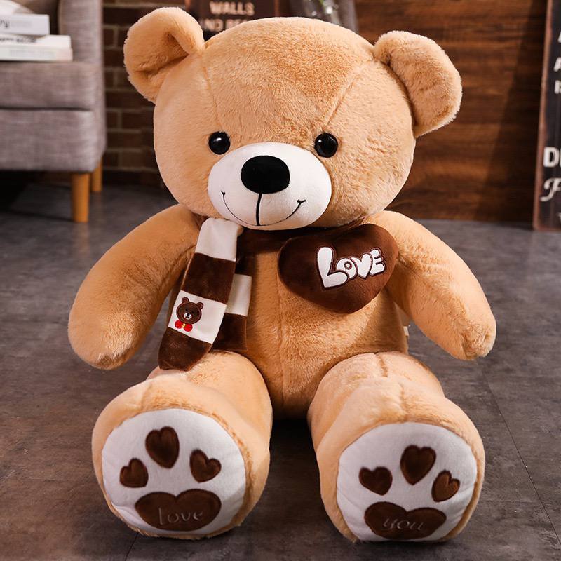 Brown teddy bear toy with a scarf and heart sitting on a floor indoors