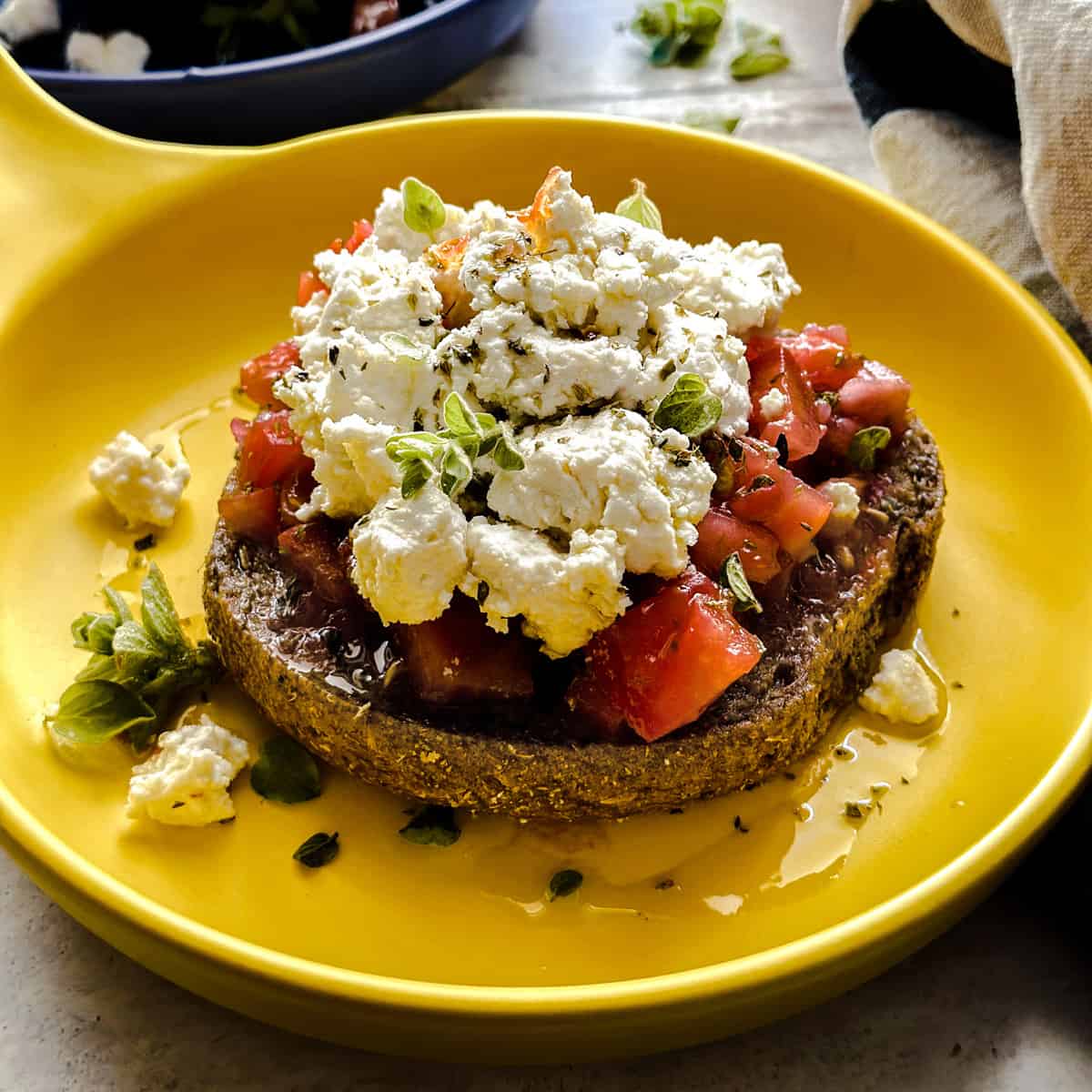 Dakos topped with tomatoes and crumbled cheese on a yellow plate