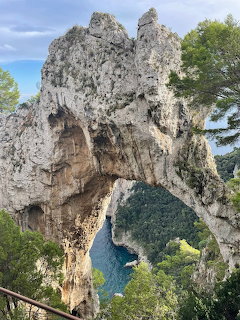 Large natural rock arch formation on Capri with turquoise sea visible through the opening and green vegetation
