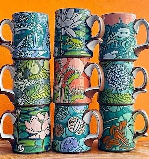 Two columns of stacked colorful ceramic mugs with hand-painted floral and nature designs on orange background