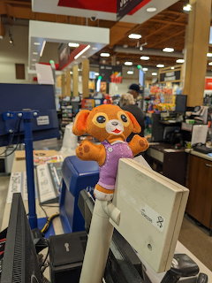 Stuffed plush dog toy sitting on a checkout counter monitor in a supermarket