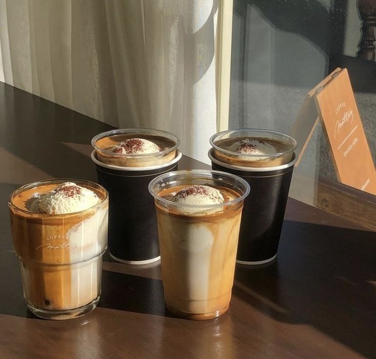 Four layered iced coffee drinks in glasses on dark table with sunlight streaming through window