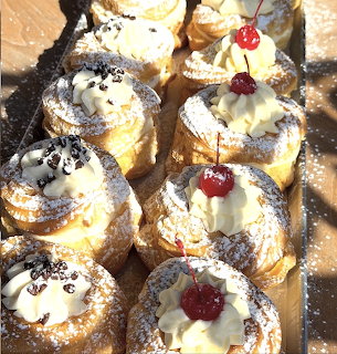 Nine cream puff pastries with whipped cream and cherry toppings arranged on a decorative tray