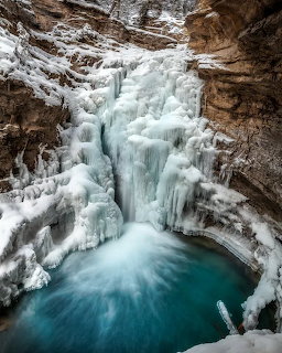 Frozen waterfall with icicles flowing into a turquoise pool inside a snowy rocky canyon