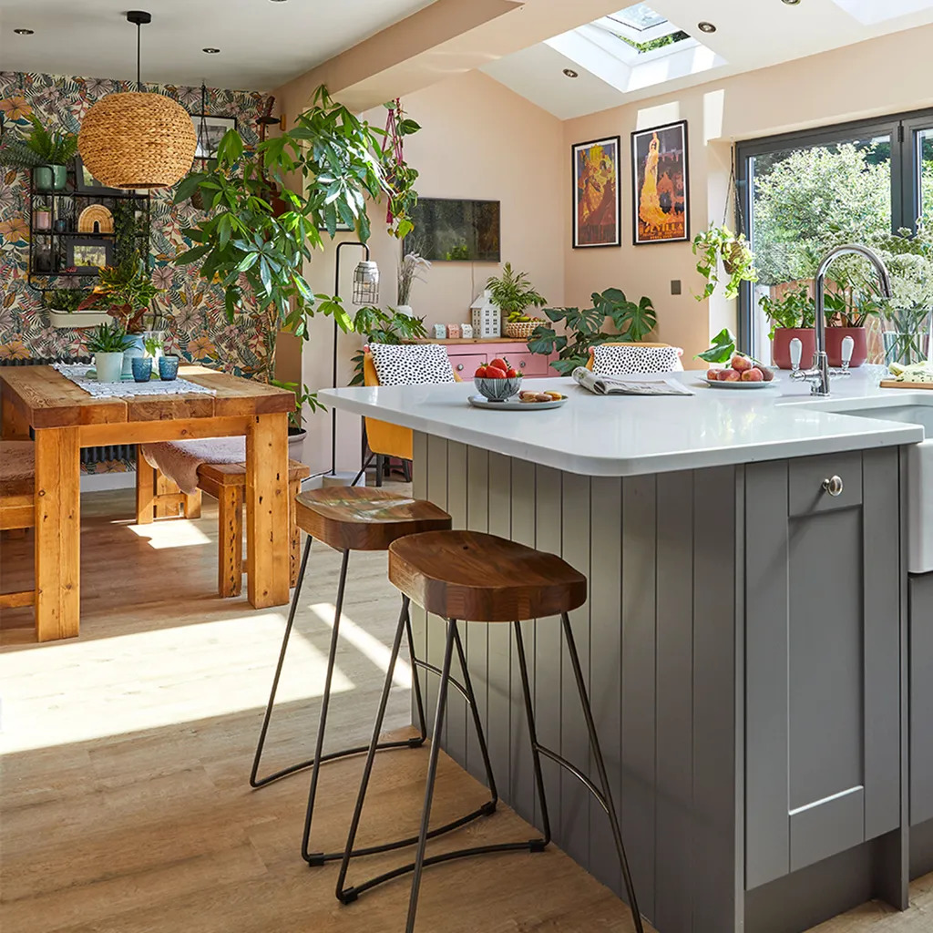 Modern kitchen with gray island, wooden table, skylights, and abundant natural light with plants