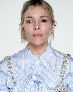 Blonde woman in blue striped blouse with crystal straps looking at camera against white background
