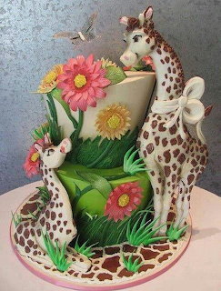 Tiered cake decorated with fondant mother and baby giraffes, flowers, leaves, and a white bow