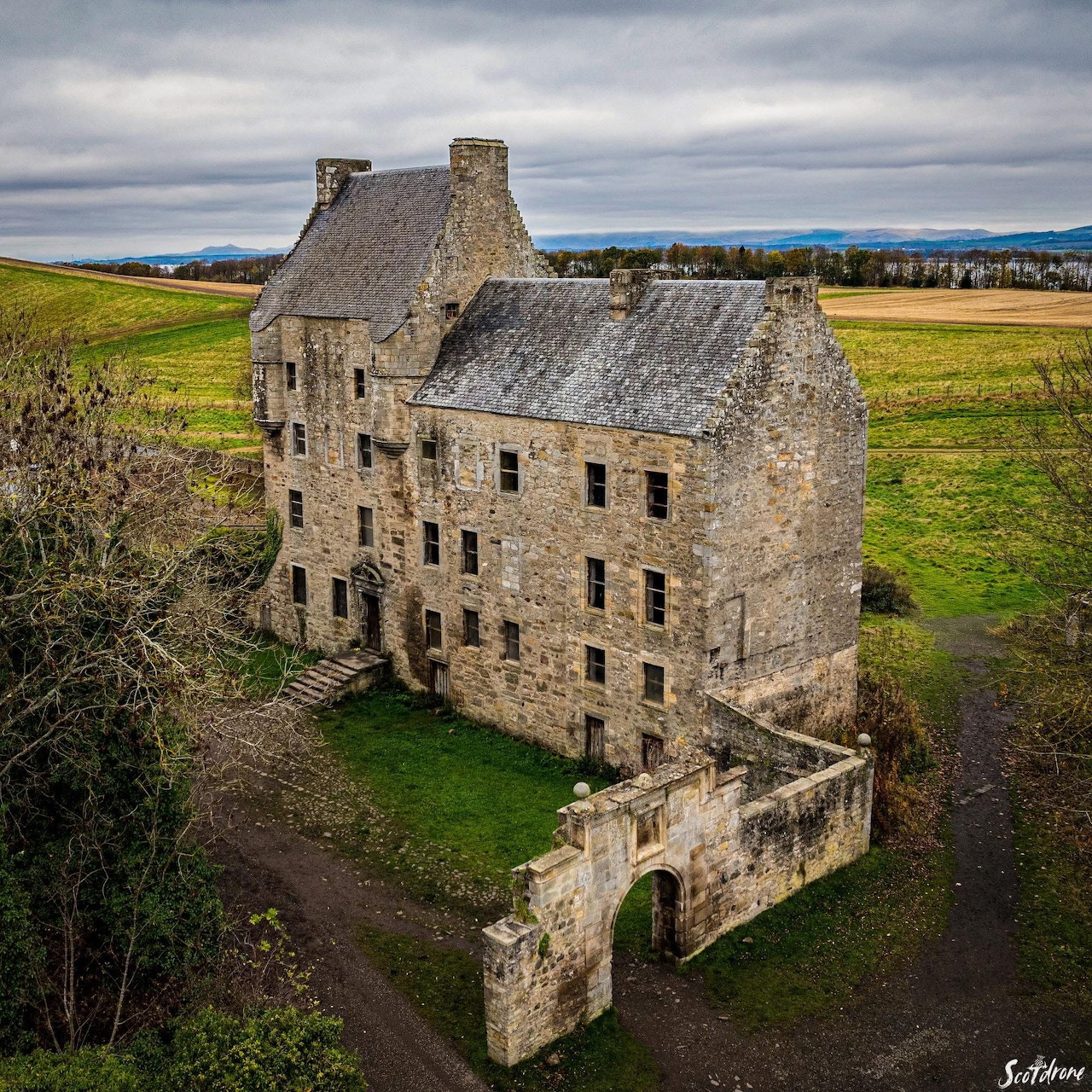 Old stone castle with an arched gate in a grassy countryside under a cloudy sky