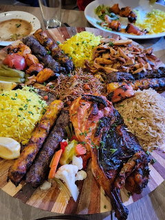 Large wooden platter of grilled kebabs, skewered meats, saffron rice, grilled vegetables, and salad