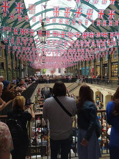 Indoor shopping arcade with many Union Jack flags hanging overhead and people on the balconies