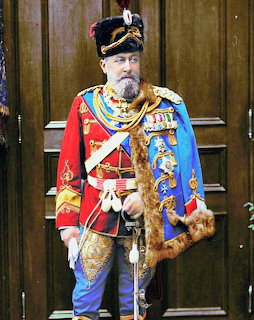 Man in ornate red and blue military dress uniform with medals and fur sporran standing by wooden doors