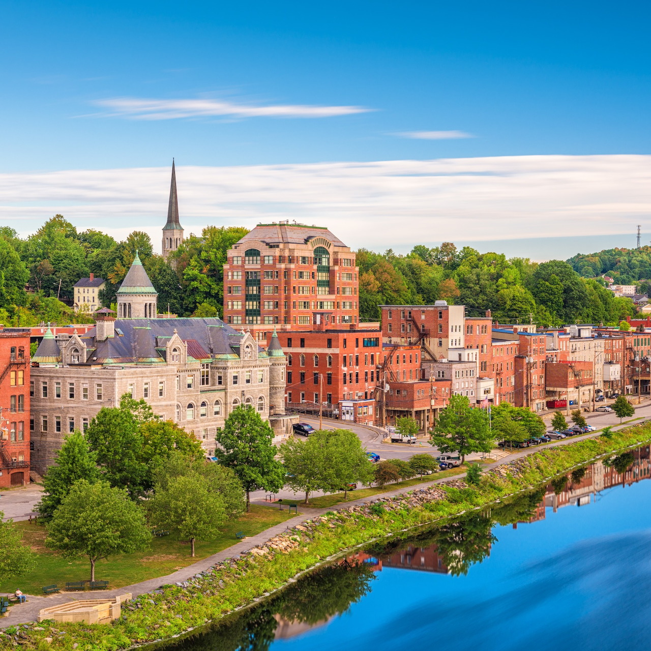 Augusta, Maine cityscape with brick buildings, church steeple, trees, and river reflection