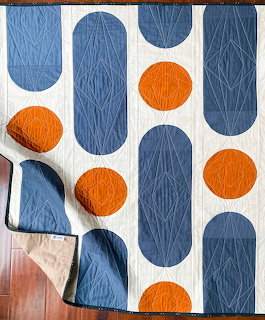 Modern geometric quilt with navy blue pill shapes and orange circles on cream fabric