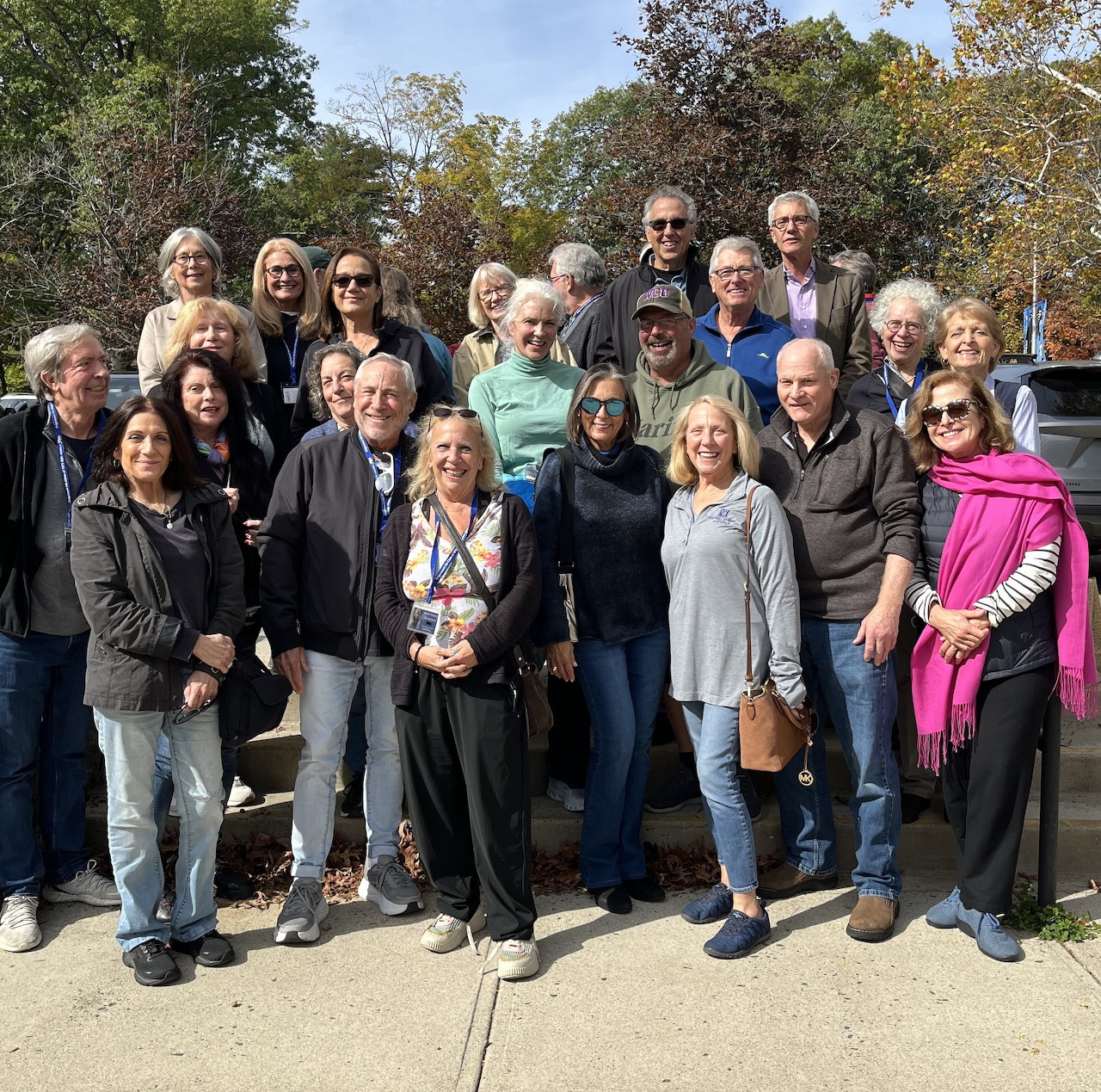 Group of adults posing together outdoors on a sunny day with trees behind them