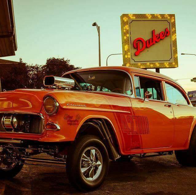 Vintage orange Chevrolet car parked under a lit Dukes sign outdoors
