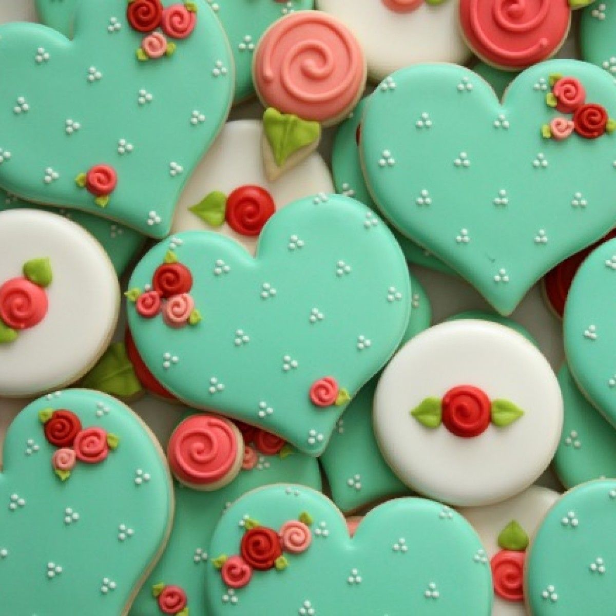 Heart-shaped and round decorated sugar cookies with teal icing, pink roses, and white dots