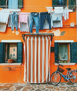 Orange Venetian house with colorful laundry drying on lines above striped door curtain and parked bicycle