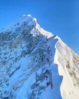Climbers ascending a steep snowy mountain ridge with rocky outcrops under blue sky