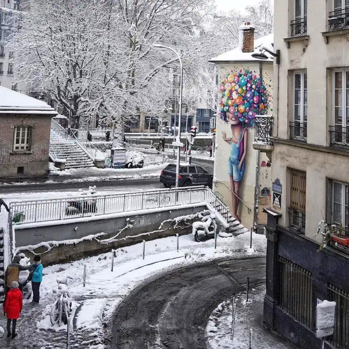 Colorful street art mural showing woman with bubble hair on building facade in snowy town square