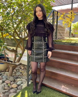Woman in black dress and sheer overlay standing on outdoor steps with plants