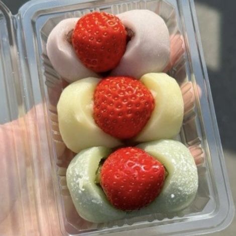 Close-up of three strawberry daifuku mochi in pink, white, and green in a clear plastic tray.