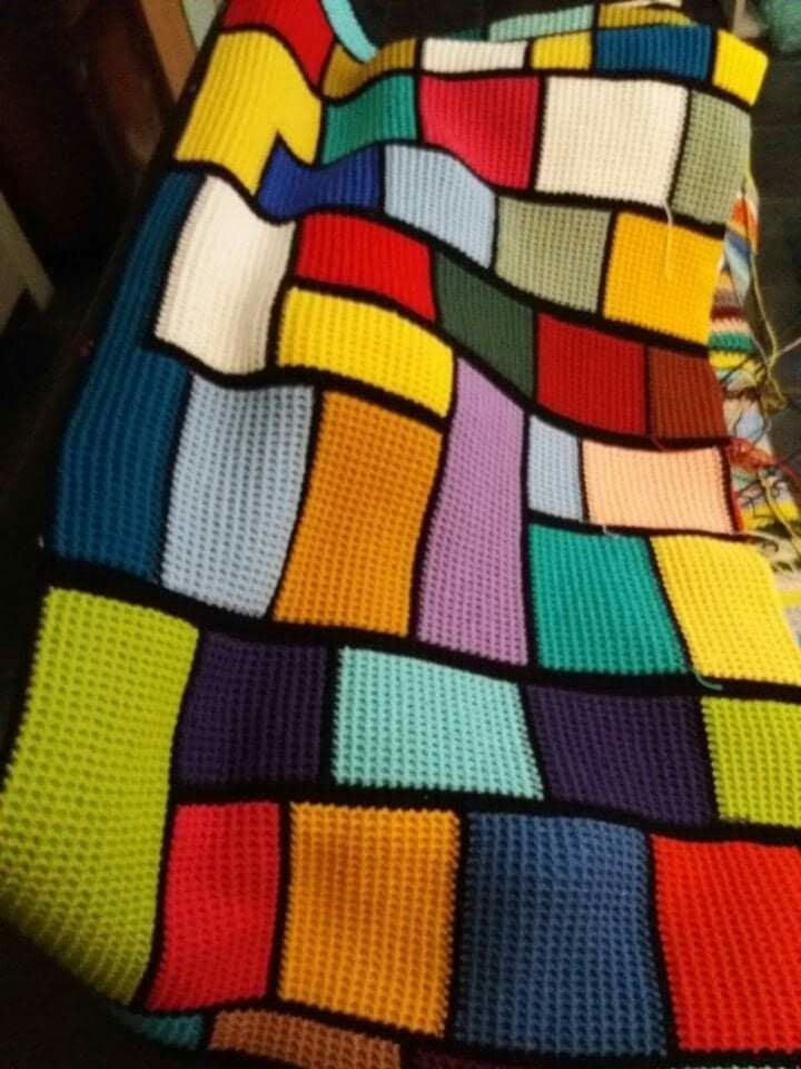 Colorful knitted patchwork blanket with geometric blocks in various bright colors draped on furniture