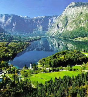 Lake Bohinj in Slovenia with mountains, green forests, and a church reflected in calm blue water