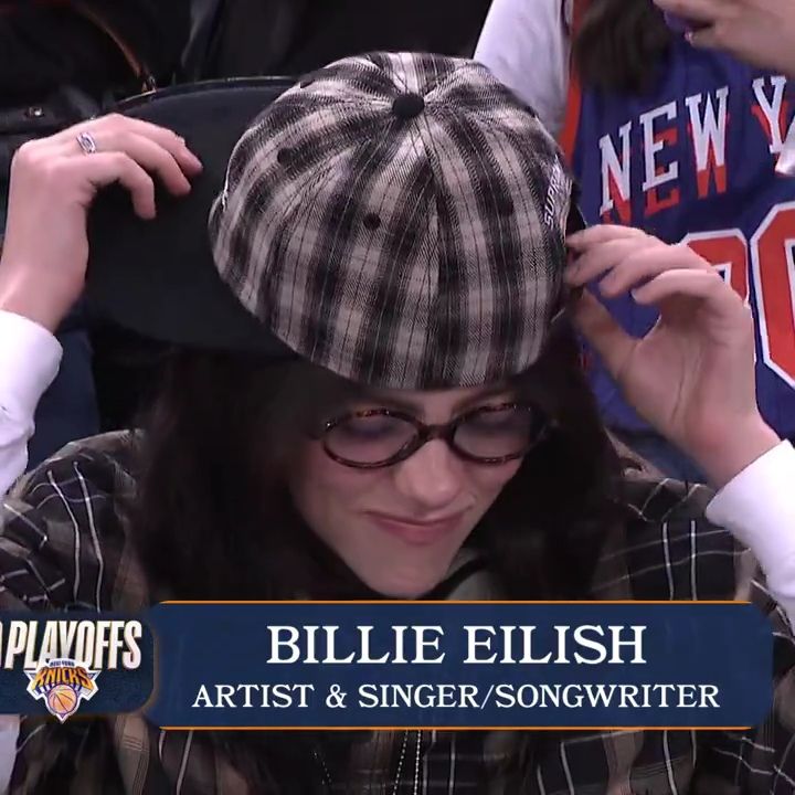 Billie Eilish in plaid cap and glasses sitting courtside at a Knicks playoff game