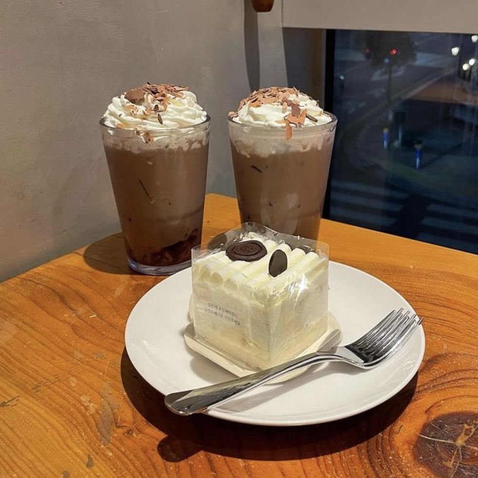 Two iced mocha drinks with whipped cream and a square cookies and cream cake on a plate