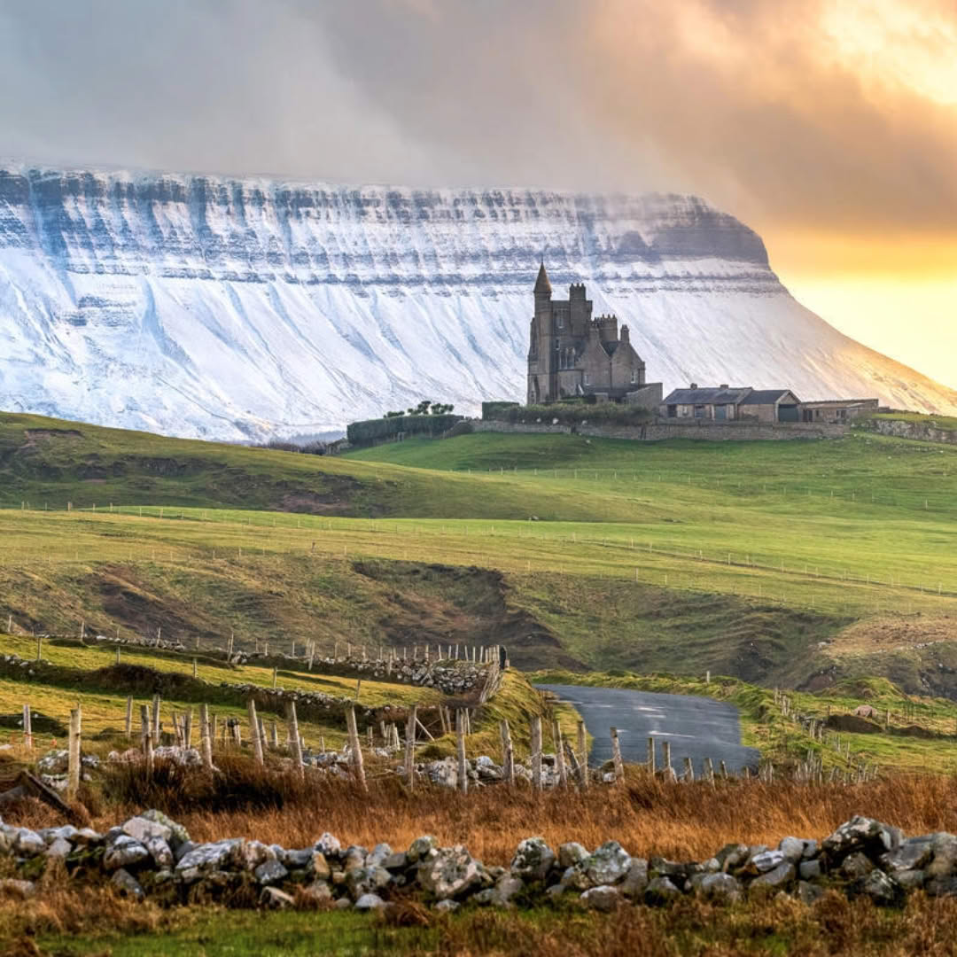 Castle in green Irish landscape beneath towering white limestone cliffs at sunset