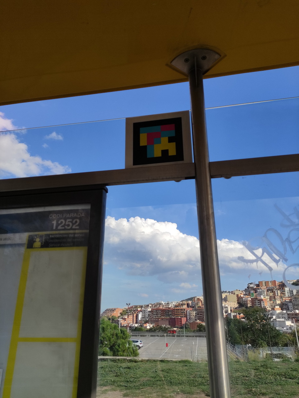 Bus stop shelter in Barcelona with route 1252 sign and colorful pixel mosaic, city buildings and river in background