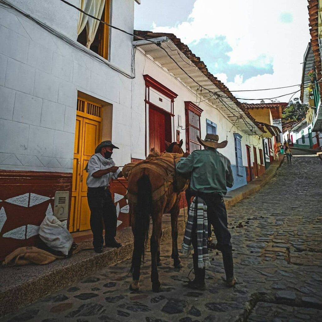 Two men and a mule on a cobblestone village street beside white buildings