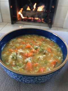 Blue bowl of chicken vegetable soup with a fireplace in the background
