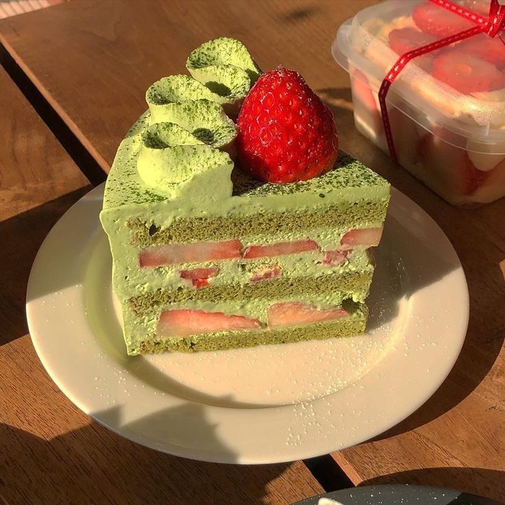 Slice of green matcha layer cake with strawberry filling and cream rosettes topped with a strawberry on white plate