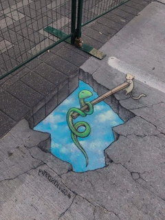 Chalk sidewalk art showing a green snake coiled around a pole above a trompe-l'oeil blue sky hole