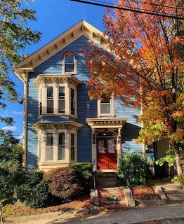 Blue Victorian house with a red front door and autumn trees in front