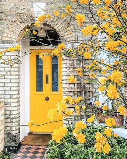 Bright yellow front door under white brick arch with yellow autumn leaves and brick walkway