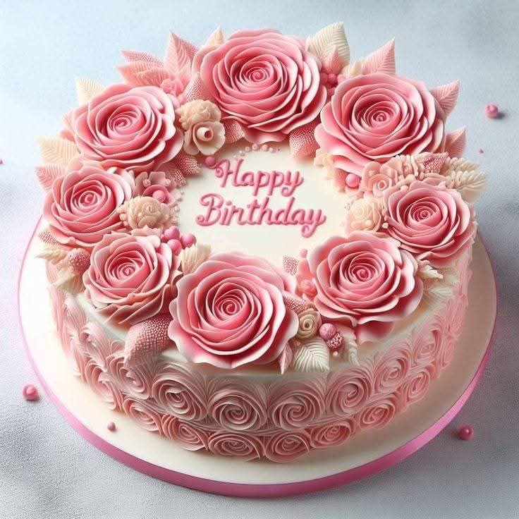 Round pink birthday cake topped with decorative paper roses and pearl accents, with 'Happy Birthday' text in center