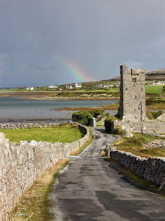 Stone tower beside coastal road with rainbow over Galway Bay, Ireland