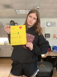 Young woman in a classroom holding a yellow handwritten poster