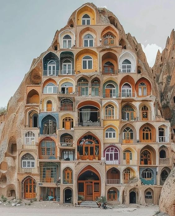 Ornate multi-story building with arched windows carved into a massive cliff under cloudy sky