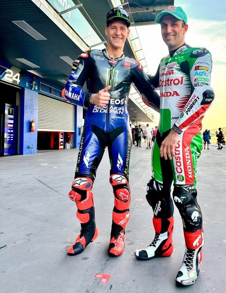 Two motorcycle racers in colorful racing suits standing in paddock