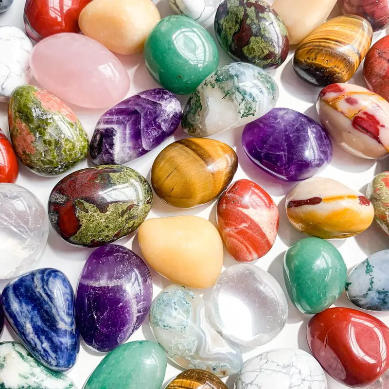 Collection of colorful polished gemstones and minerals arranged on white surface
