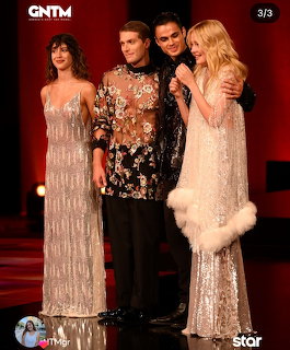 Four models posing on stage in elegant gowns at a GNTM fashion show finale with red lighting