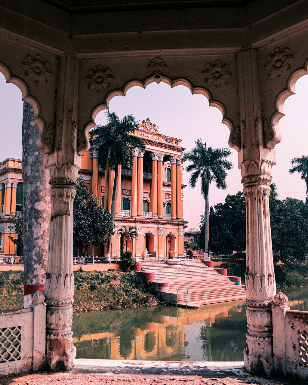 Ornate Indian palace with decorative arches, reflecting pool, and palm trees at sunset