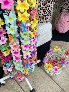 Colorful tropical flower leis hanging on a rack outdoors with a wicker flower basket nearby