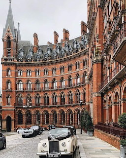 Red brick Victorian Gothic railway station with ornate arched windows and vintage black taxi cabs parked in front