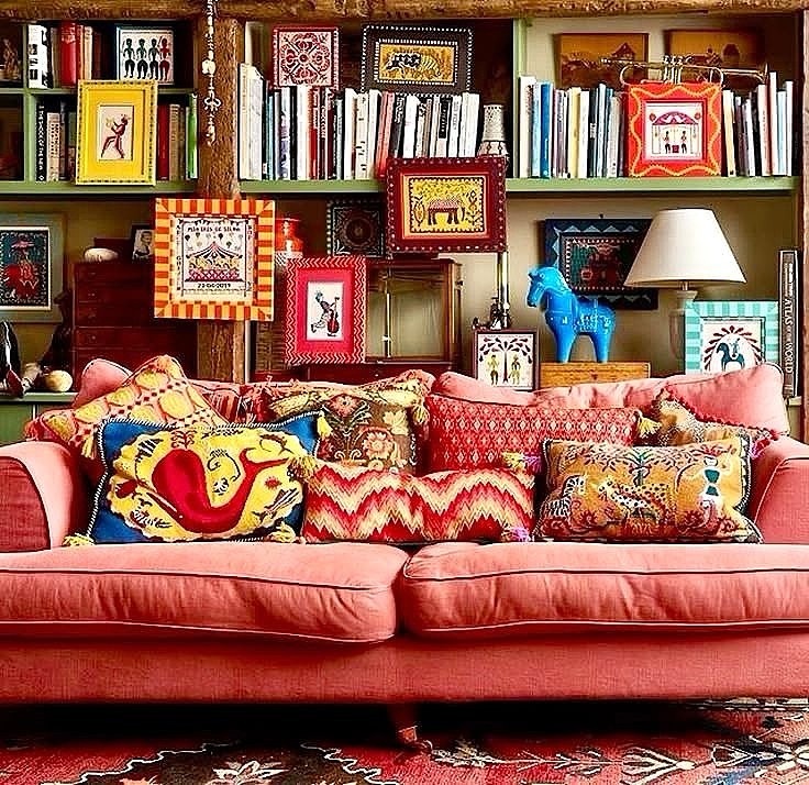 Coral sofa with colorful pillows in front of bookshelf with books and framed artwork
