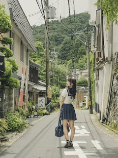 Young woman in school uniform standing on a quiet Japanese town street with green hills in background