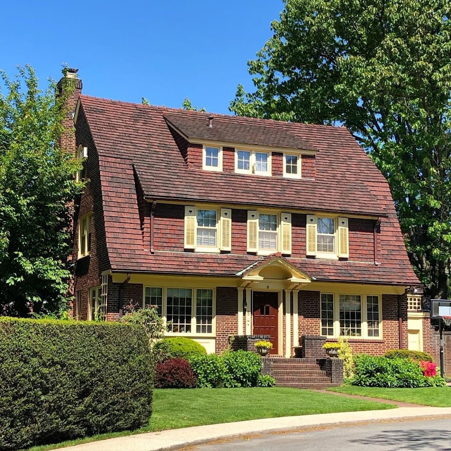 Three-story Tudor-style house with red tile roof and manicured front lawn